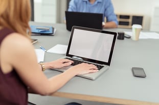 Modern business office where employees, man and woman, work on laptops and keep documents, files and mobile phones on the same shared desk